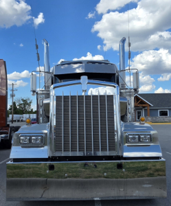 Kenworth W900 front view showing chrome grille, side exhaust stacks, rectangular headlights, and bumper.