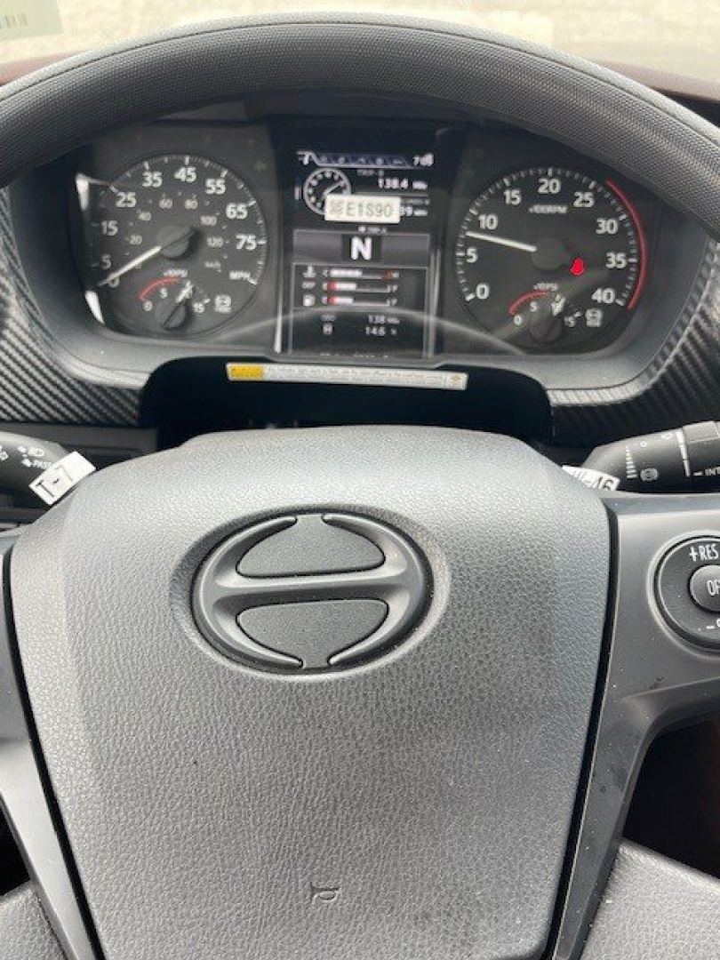 Dashboard of a 2027 Hino L7 hooklift truck showing instrument cluster with speedometer, tachometer, and center display. Steering wheel with Hino logo visible.