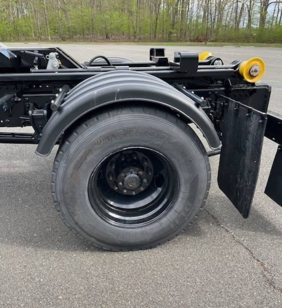 Hino L7 hooklift truck chassis side view showing rear wheel and fender with hydraulic components and frame rails.