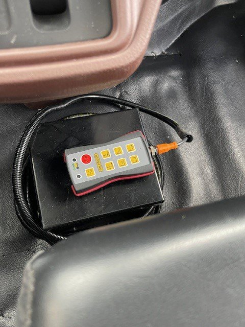 Hino L7 hooklift truck interior showing a compact remote control with yellow buttons and orange connector, placed on a dashboard area.