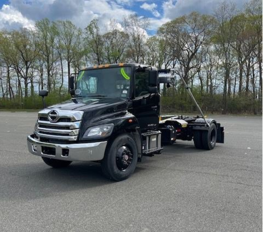 Hooklift truck cab in profile view showing black Hino L7 chassis with chrome front bumper and extended wheelbase, no. 5PVNV7DR2V5T50054 visible on truck.