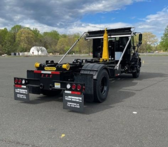 Truck rear view showing hooklift undercarriage and hydraulic arms ready for loading on a Hino L7 chassis.