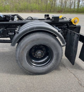 Hino L7 hooklift truck chassis side view showing rear wheel and fender with hydraulic components and frame rails.