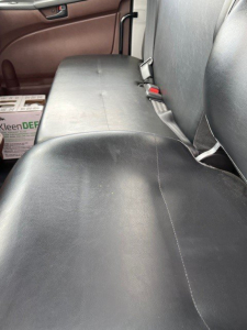 Truck interior rear seating area in a Hino L7 showing black vinyl bench seat with seat belts and a box of Kleen-DEF in the background.