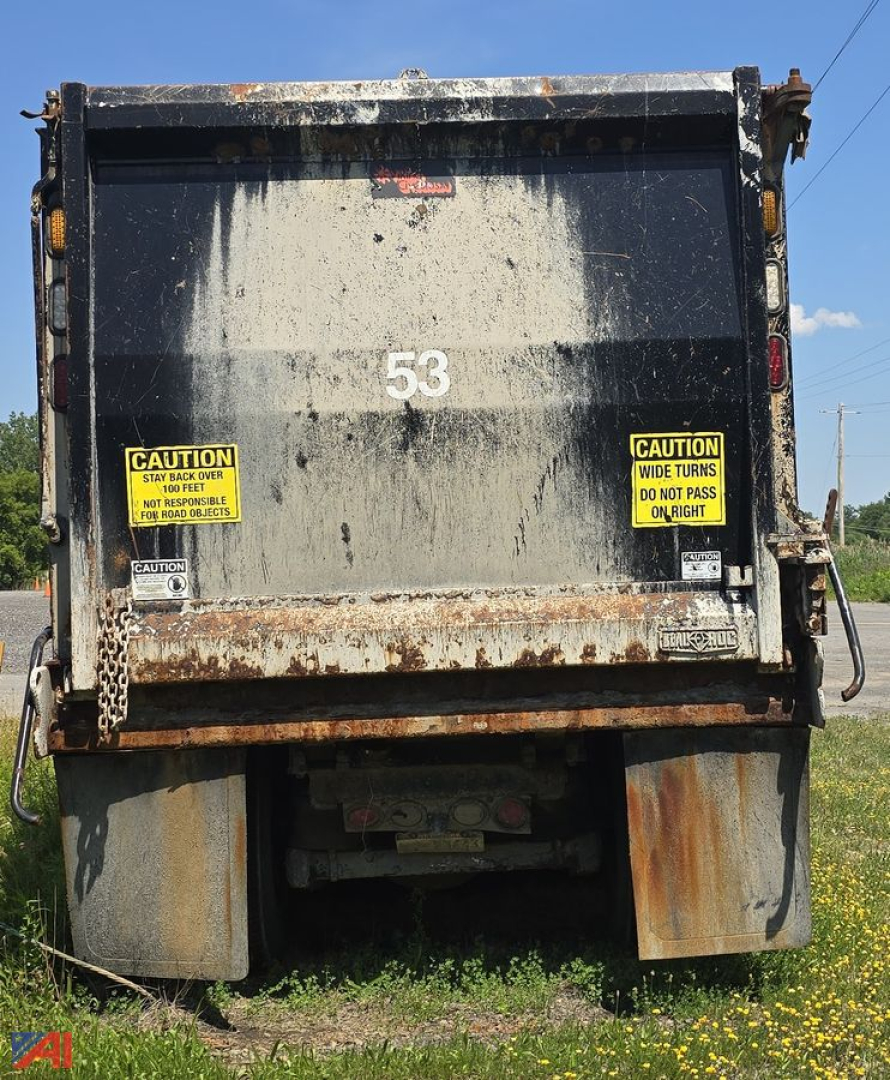 Dump truck rear showing large number 53 on tailgate with caution labels on both sides and rusted lower edge.