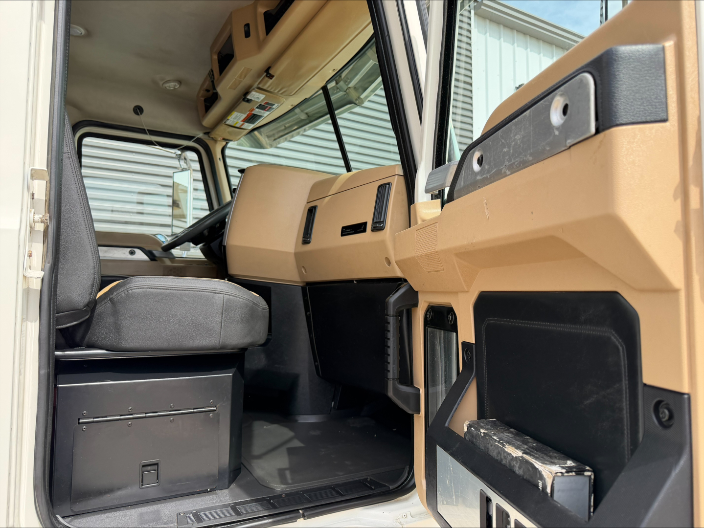 Cab interior of 2019 Mack PI64T daycab showing tan dashboard and driver seat with control panels.