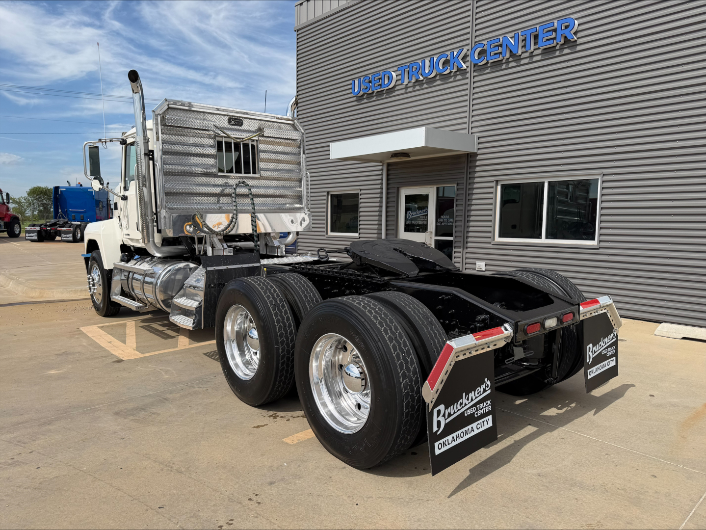 2019 Mack PI64T tractor showing rear view with dual rear axles, metal exhaust/stack, and fifth-wheel, in front of used truck center building.