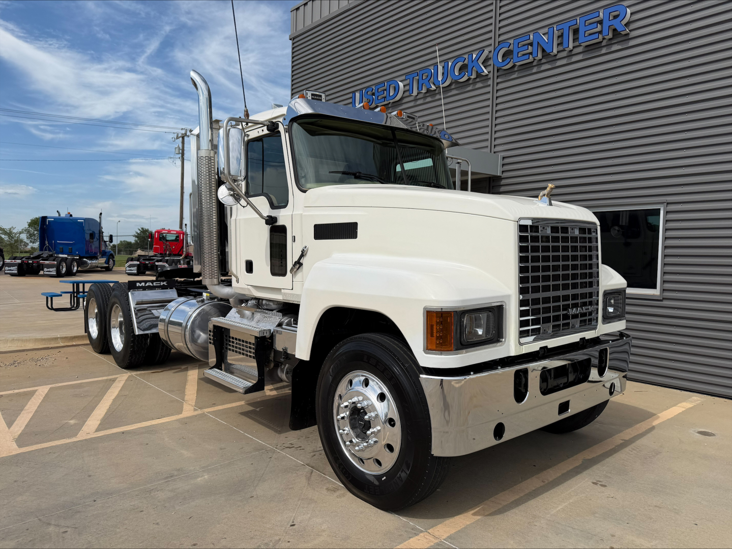 Mack PI64T conventional daycab truck in white viewed from front-right with chrome exhaust stacks, parked outside a used truck center.