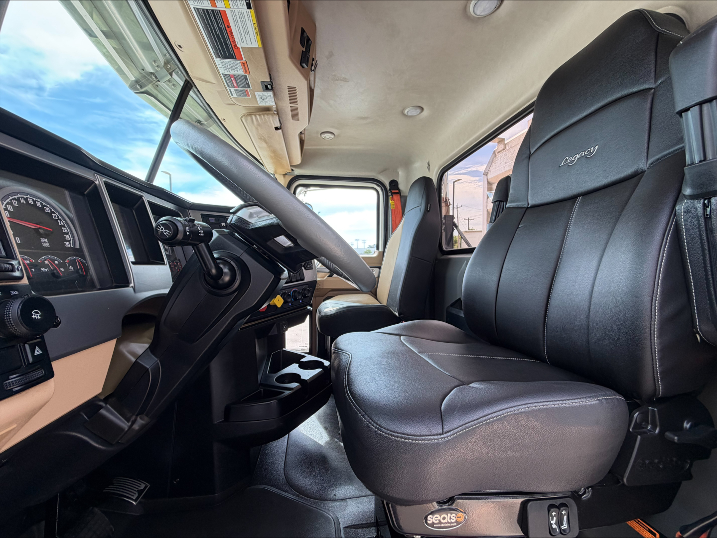 Cab interior of a 2019 Mack PI64T daycab showing steering wheel, dashboard gauges, driver seat, and passenger seat with Seals quilted upholstery.