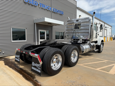2019 Mack PI64T truck tractor in front of used truck center showing tandem rear axles and chrome fuel tanks.
