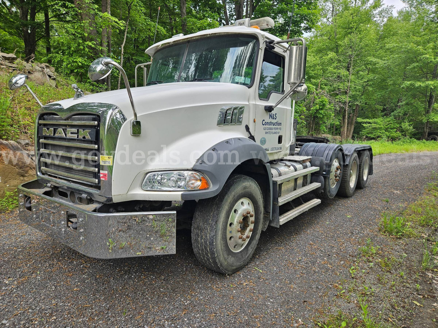 Mack GU813 truck in white, front-left view showing grille, bumper, headlights, and dual rear axles; company logo on door and exterior mirrors