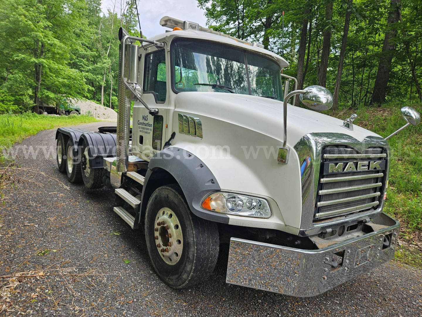 Mack GU813 truck in side angle showing front grille, headlights, chrome bumper, and dual mirrors.