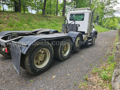 Mack GU813 tractor truck chassis and cab in a wooded lot, side view showing rear dual wheels and fifth wheel.