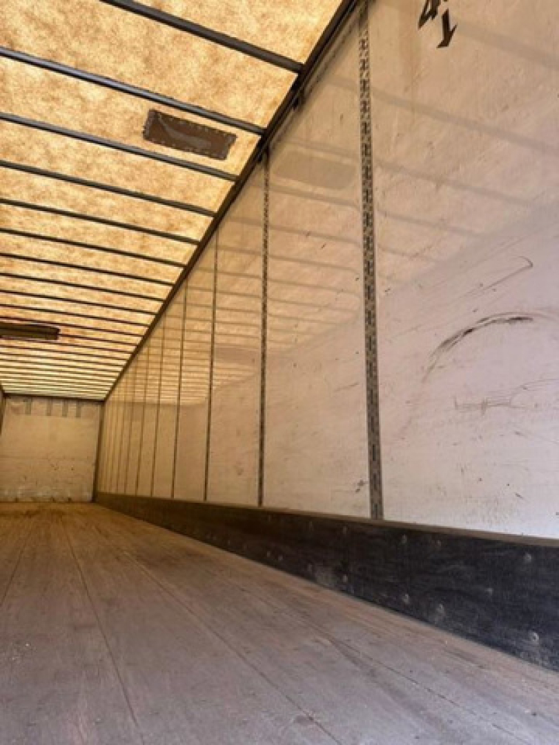 Trailer interior showing wooden floor and white insulated side walls with vertical support rails.