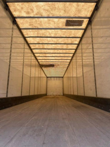 Trailer interior showing long cargo area with wooden floor, light panels on ceiling, and side walls with vertical ribs.