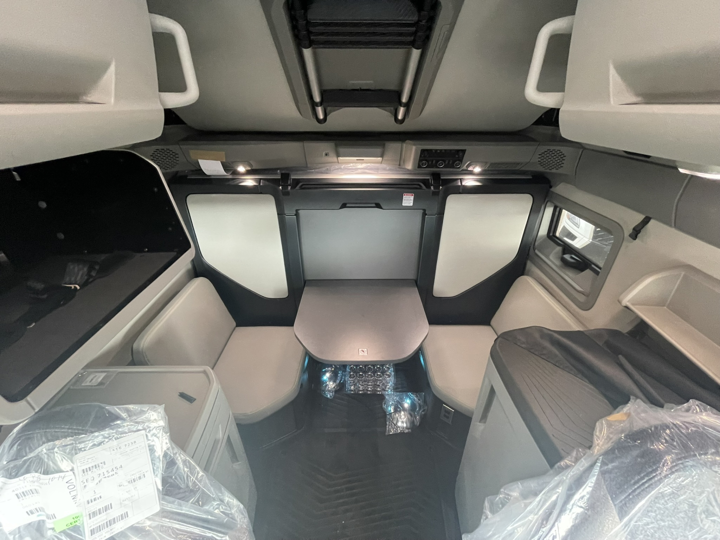 Interior view of a new 2026 Volvo VNL64T860 sleeper cab showing seating area, table, overhead storage, and cabin fixtures.