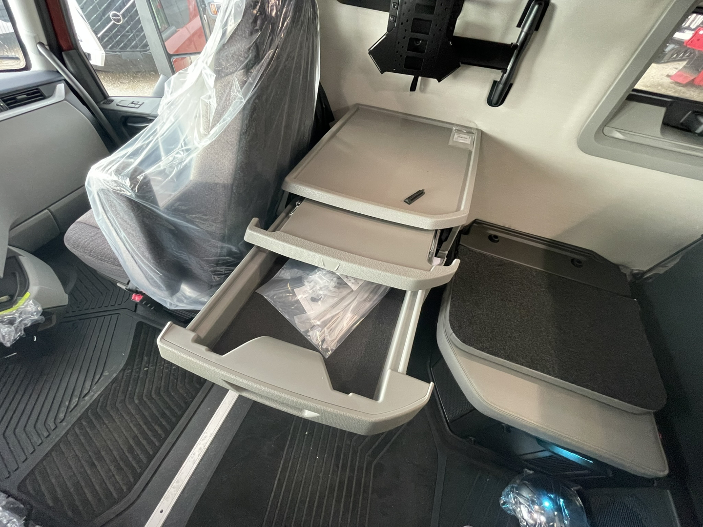 Volvo truck interior showing multi-level fold-out storage drawers in the cabin with gray trays and a small table, driver seat with plastic cover.