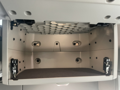 Truck cab storage compartment empty drawer in Volvo VNL64T860 engine bay area showing interior of glovebox with mounting holes and latches.