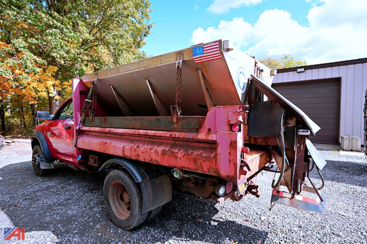 Dump bed of a 2011 Dodge Ram 5500HD dump truck with red cab and scattered metal components; American flag on the bed; gravel surface.