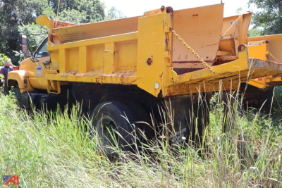 Side view of a yellow 1993 Chevrolet Kodiak C7500 dump truck in a grassy lot, showing the dump body and dual rear wheels.