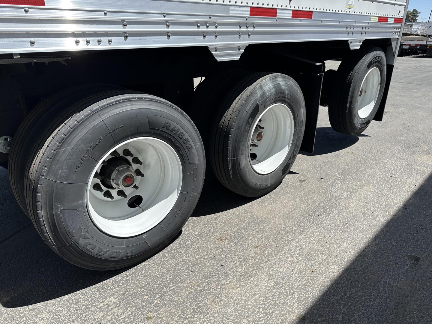 Triple-axle trailer wheelset with white rims and black tires, portion of the side and undercarriage of a metal hopper trailer.