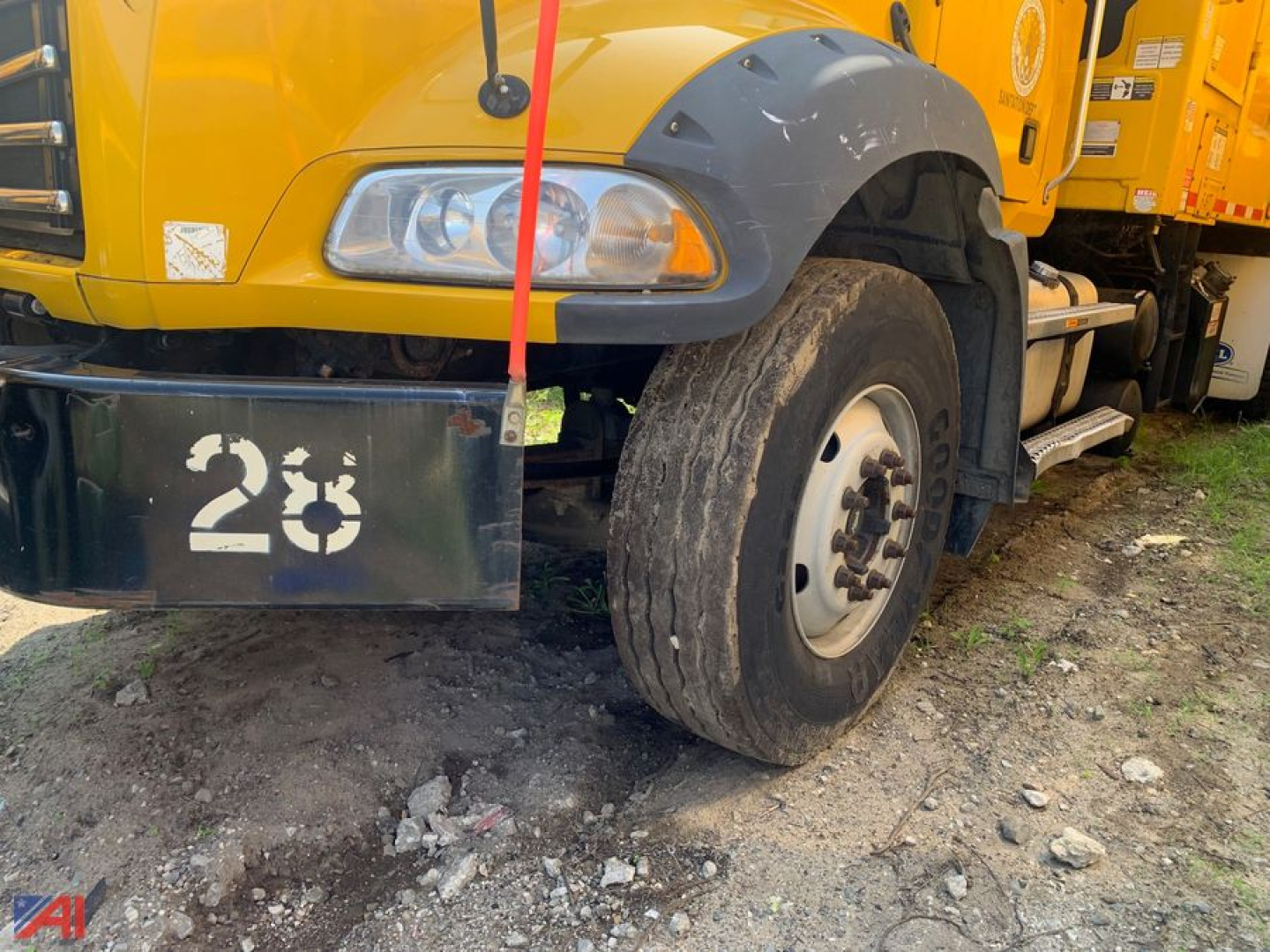 Front left view of a yellow Mack garbage truck showing front wheel and bumper with the number 23 on the bumper.