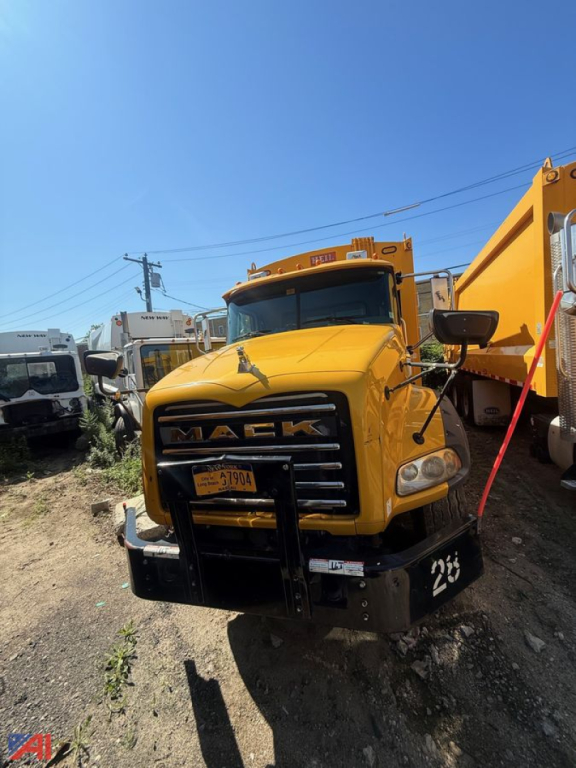 Yellow 2014 Mack garbage truck front view with front bumper guard and side mirror; visible license plate and large cargo bed at rear.