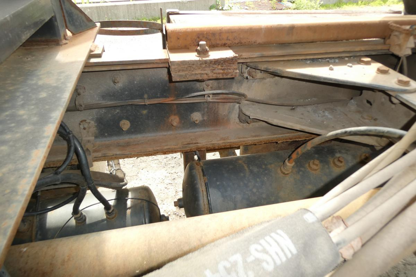 Vehicle chassis and engine bay of a Kenworth T800 roll-off truck showing metal frame, hoses, and a hydraulic component.