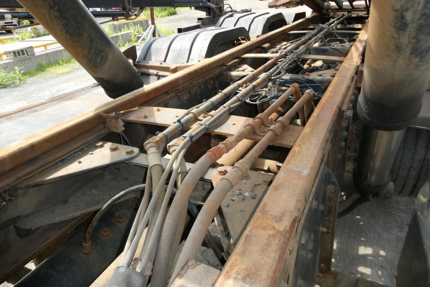 Kenworth T800 chassis frame with hydraulic lines and hydraulic components in view, rust-colored metal rails and piping along the truck frame.