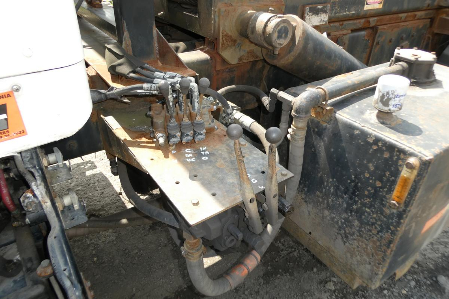 Kenworth T800 control levers and hydraulic wiring on a rolloff truck, with rusty metal, hydraulic hoses, and operator levers visible near the cab area.