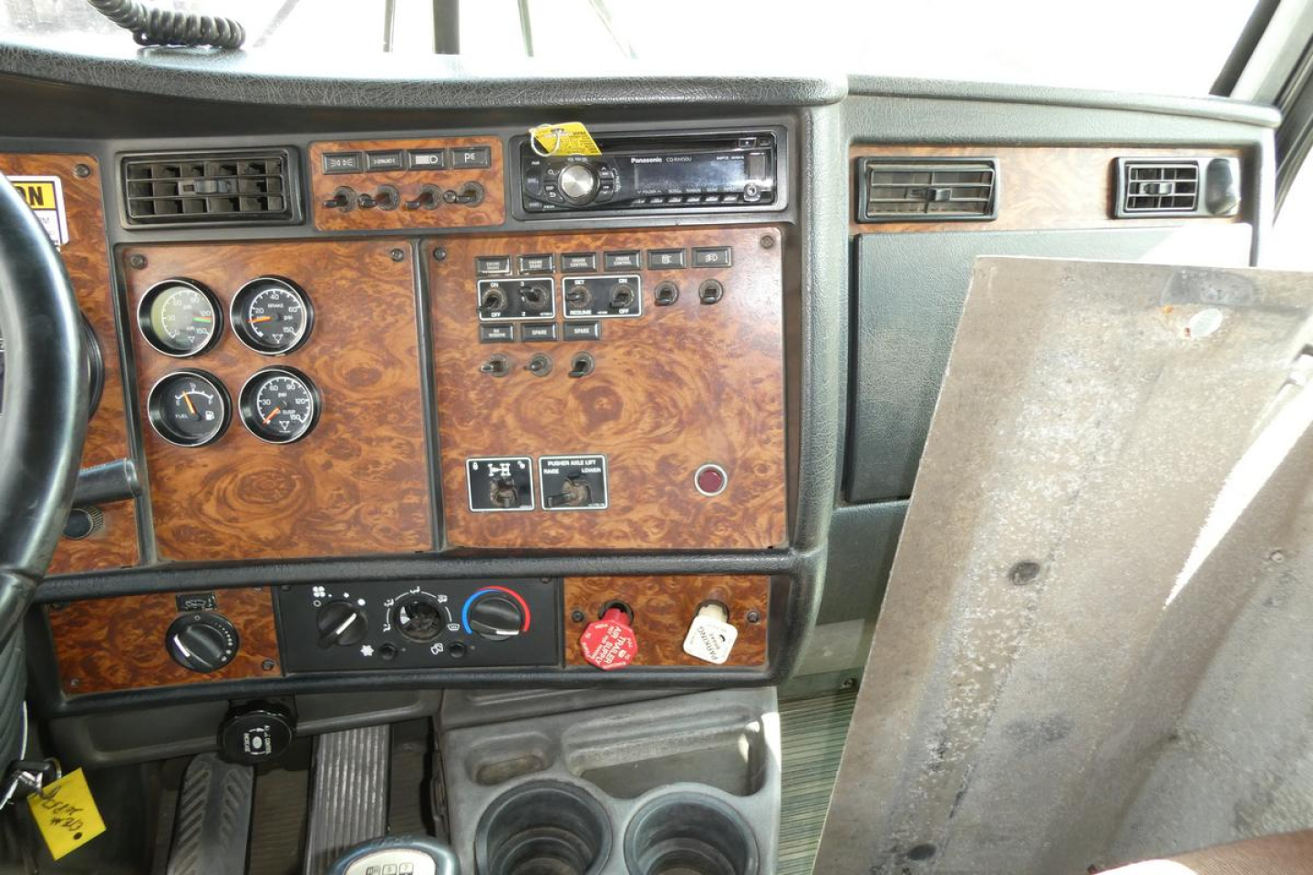 Kenworth T800 dashboard panel with woodgrain finish, gauges, controls, and a metal panel door to the right.