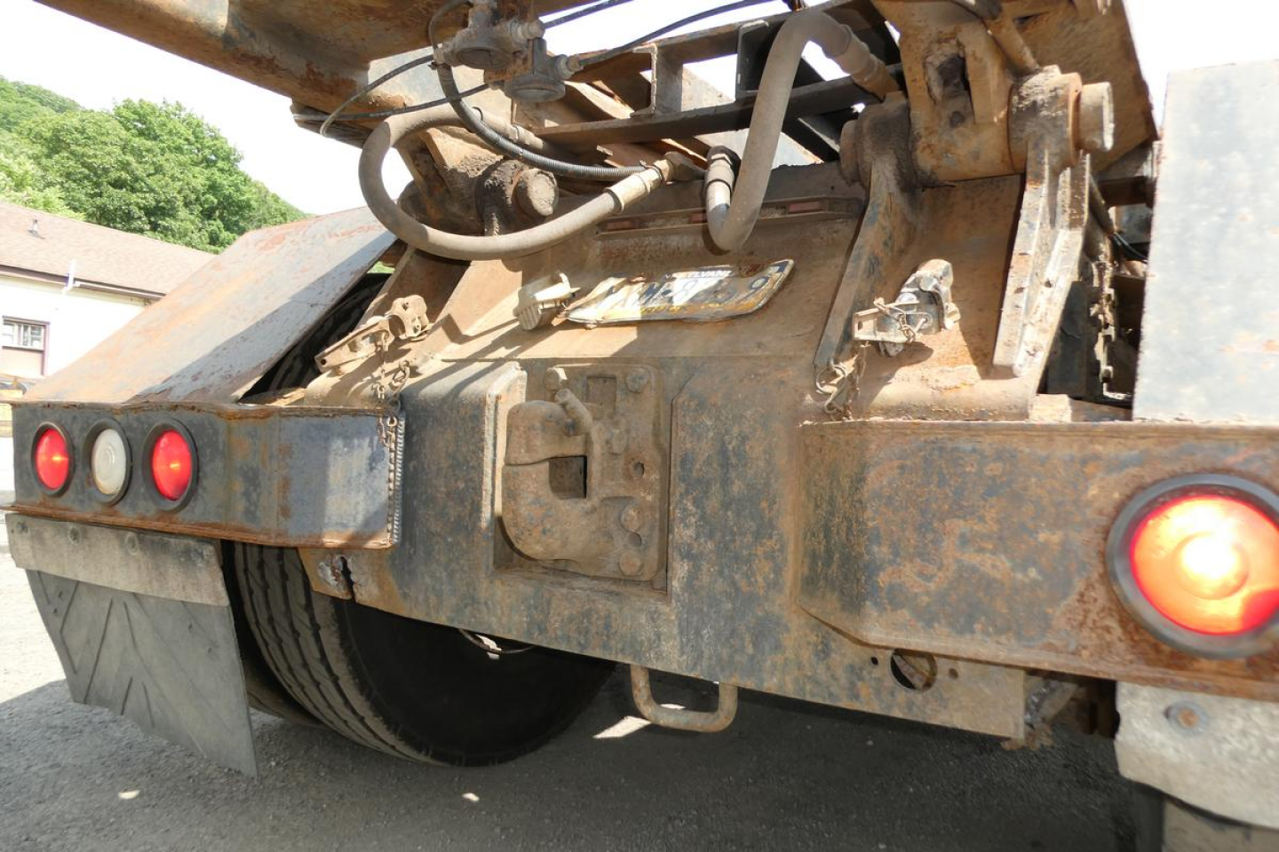 Rear view of a 2003 Kenworth T800 roll-off truck showing rusty brown chassis, taillights, and hydraulic system components under a dump bed.
