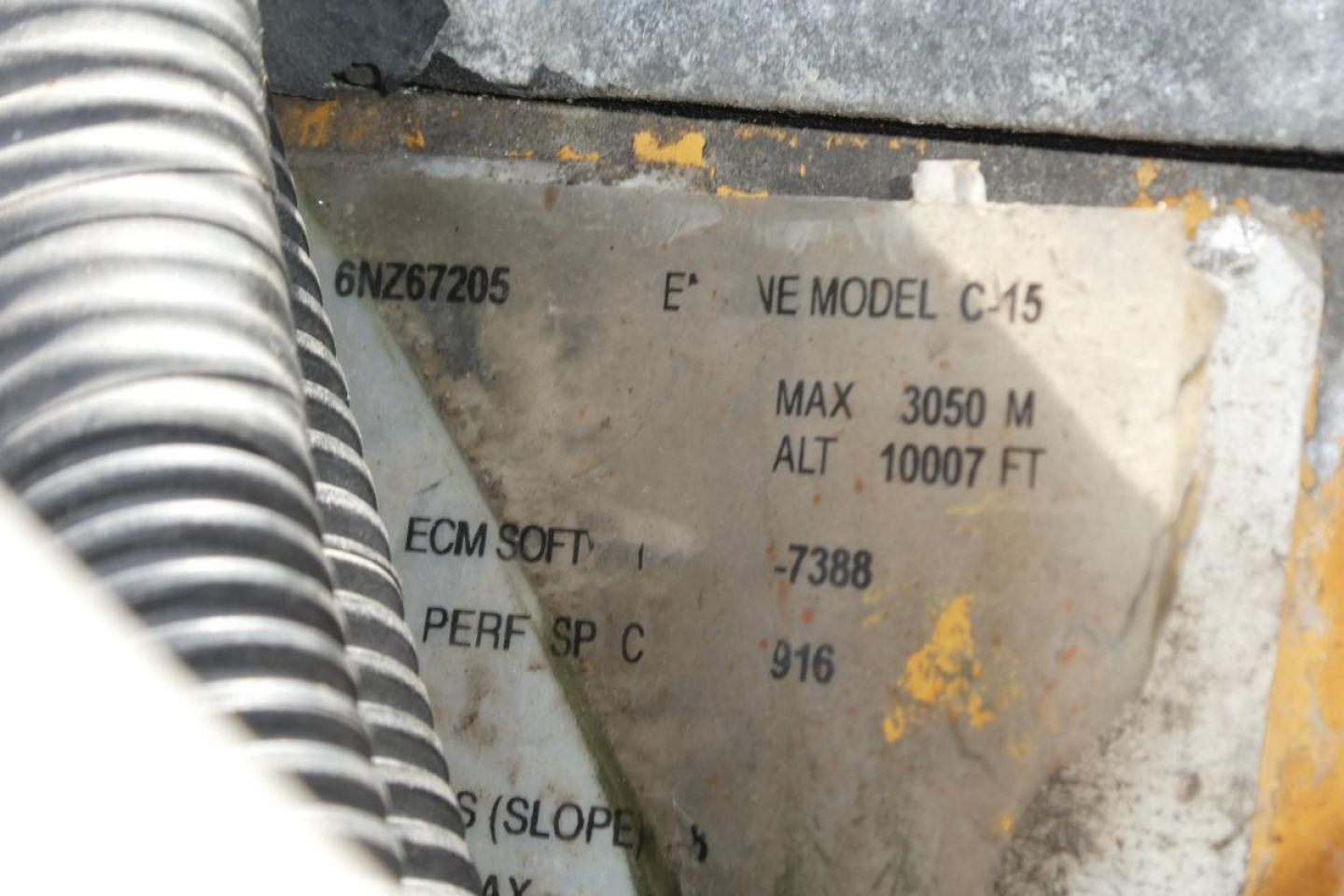 Kenworth T800 rolloff truck interior label showing model and specs plate with numbers 6NZ67205, E? MODEL C-15, MAX 3050 M ALT 10007 FT, ECM SOFT, PERF SP C 916, worn plate behind flex conduit