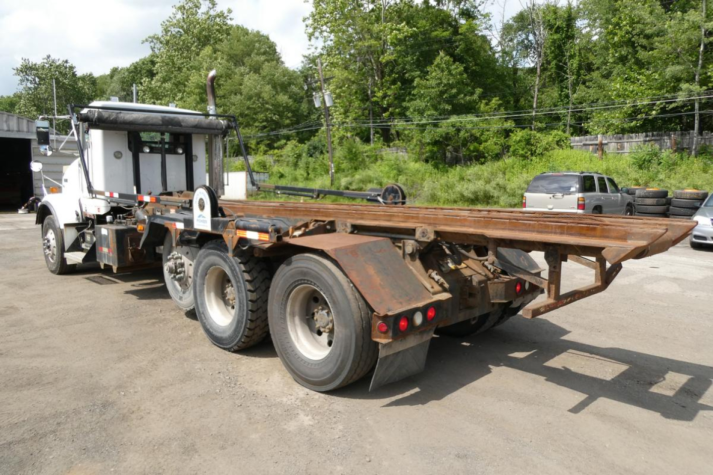 Kenworth T800 rolloff truck rear/side view showing long flatbed with rusted frame and dual rear axles.