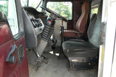 Kenworth T800 cab interior showing steering column, dashboard, and driver seat with dust and wear in a roll-off truck.