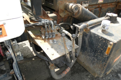 Kenworth T800 control levers and hydraulic wiring on a rolloff truck, with rusty metal, hydraulic hoses, and operator levers visible near the cab area.