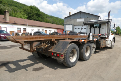 Kenworth T800 roll-off truck with flatbed and hydraulic system in view, rear tires and chassis visible