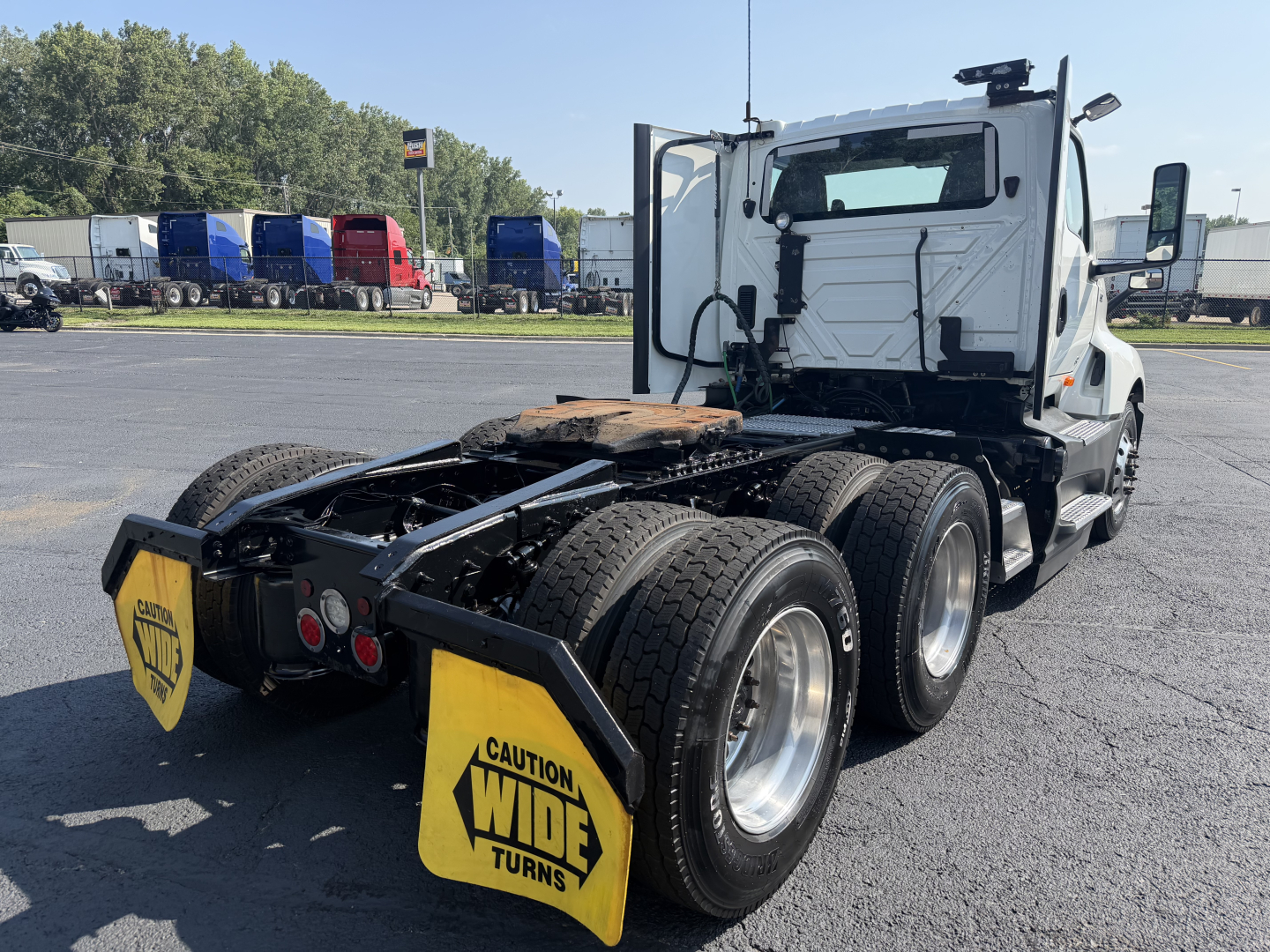 International LT625 tractor showing rear chassis and dual rear axles with wide turns warning signs and cab in background.