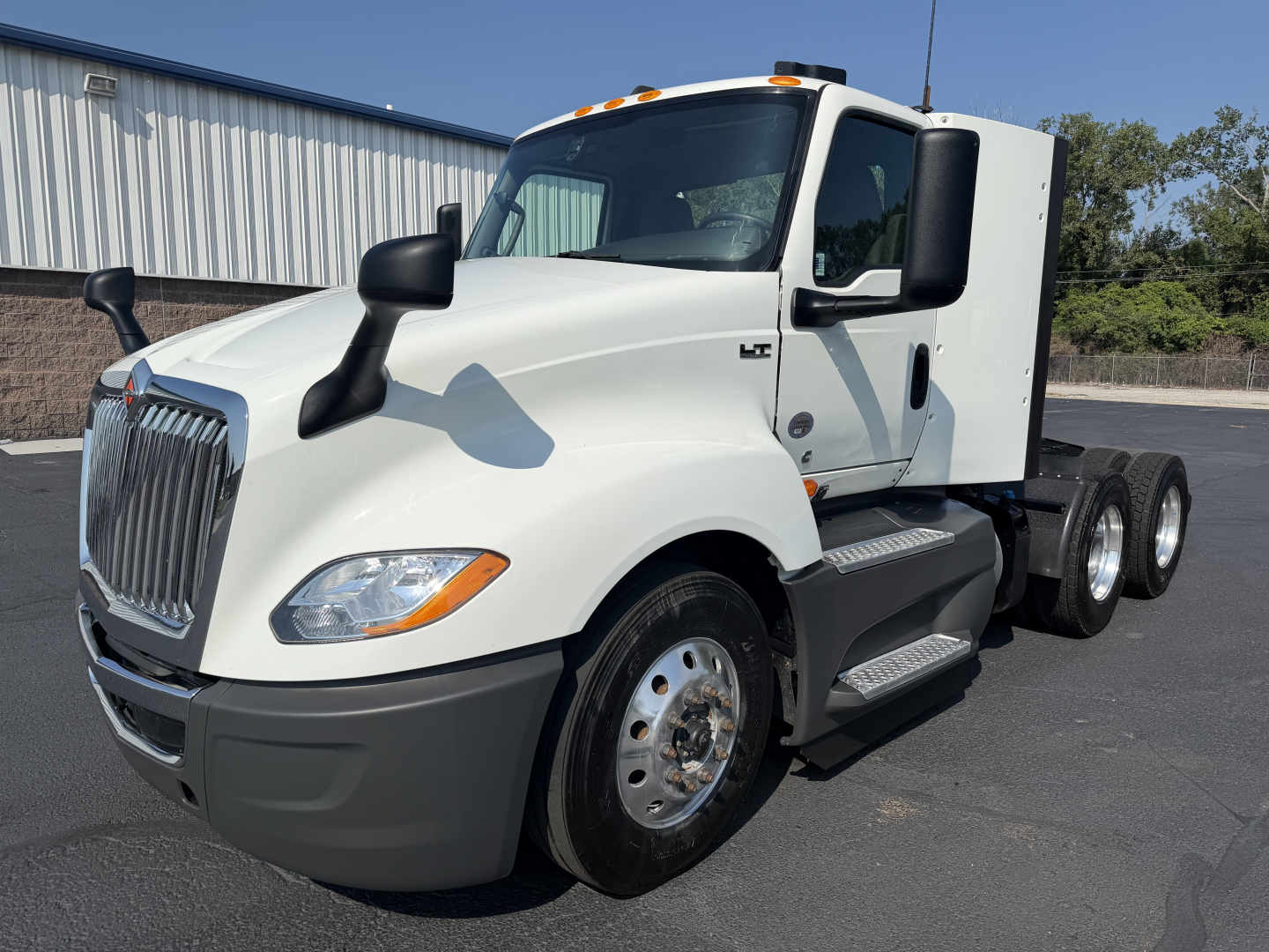 Truck cab side view with white International LT625, dual rear axles, black mirrors, and chrome front grille. Visible headlights, front bumper, and side steps.