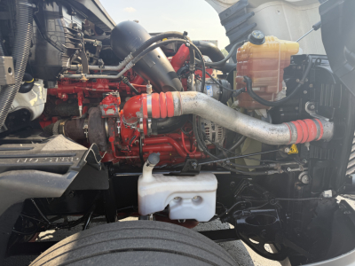 Truck engine bay with red engine, white coolant reservoir, and yellow fluid bottle. Visible hoses and metal components.