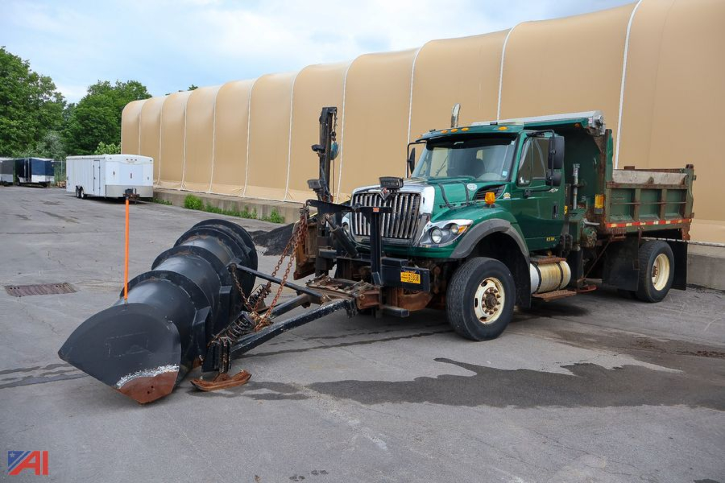 International WorkStar 7600 dump truck with front plow attachment, green cab, large snow/plow blade in front.