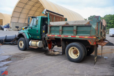 International WorkStar 7600 dump truck with green cab and worn green bed, side view parked on concrete.