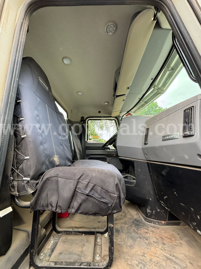 Truck interior cabin of a 2020 Mack Granite 64BR MHD showing driver seat and dashboard with Mack badge; vinyl seat cover, dirt floor, overhead ceiling, single cab layout.