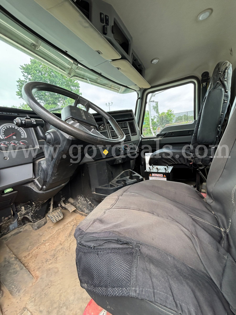 Truck cab interior showing steering wheel, dashboard, and driver seat with seat cover in a Mack Granite 64BR MHD.