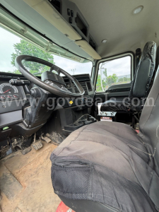 Truck cab interior showing steering wheel, dashboard, and driver seat with seat cover in a Mack Granite 64BR MHD.