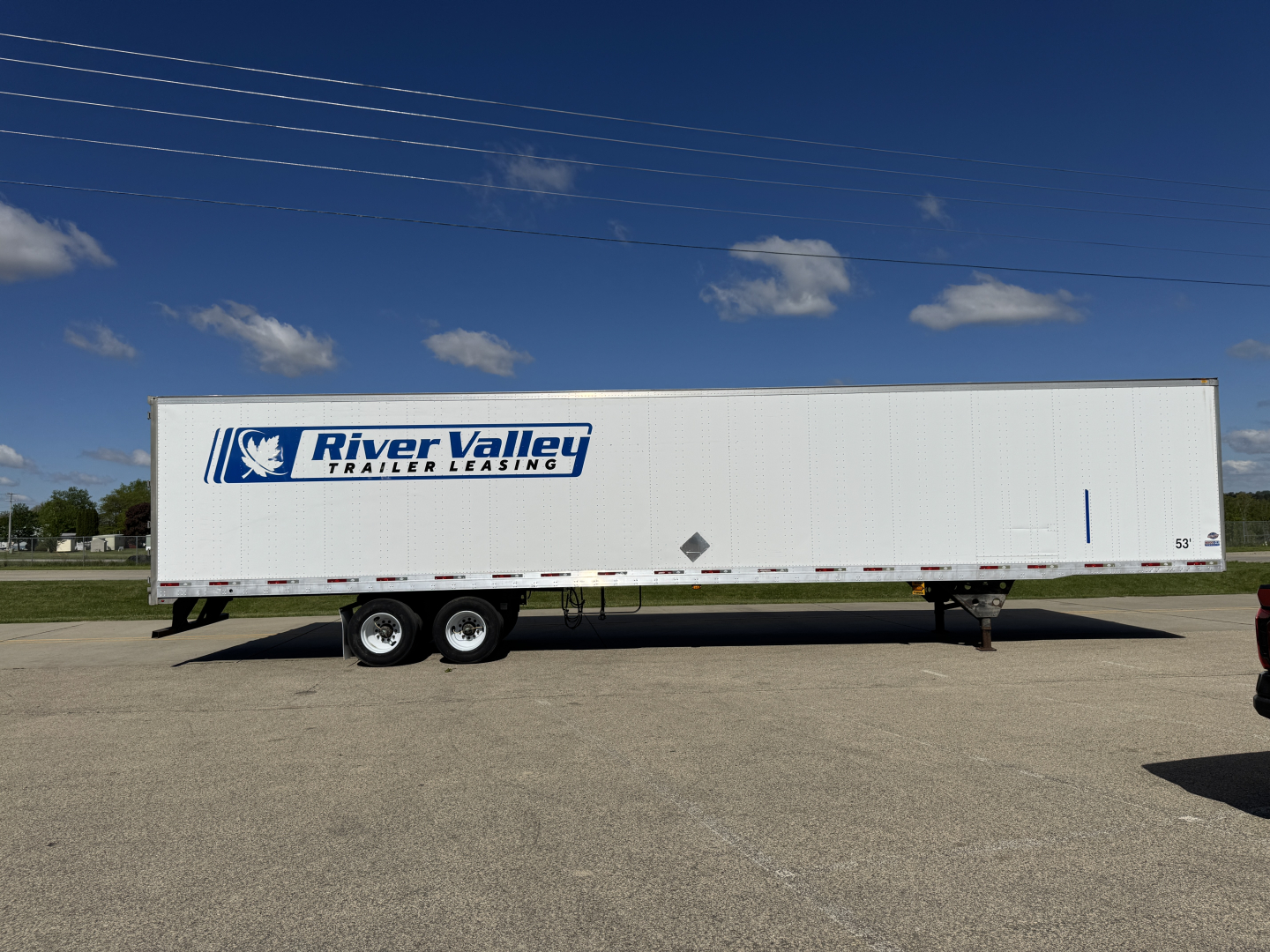 Trailer side showing River Valley Trailer Leasing logo, long white utility trailer with dual rear axles, blue sky.