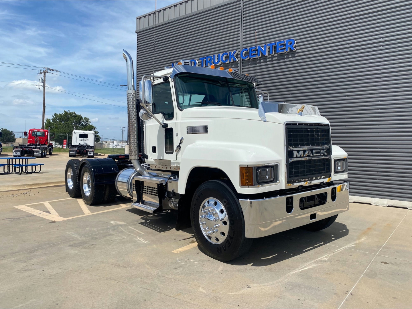 2021 Mack PI64T conventional daycab truck in white, front three-quarter view, parked outside dealership with 'TRUCK CENTER' sign in background.