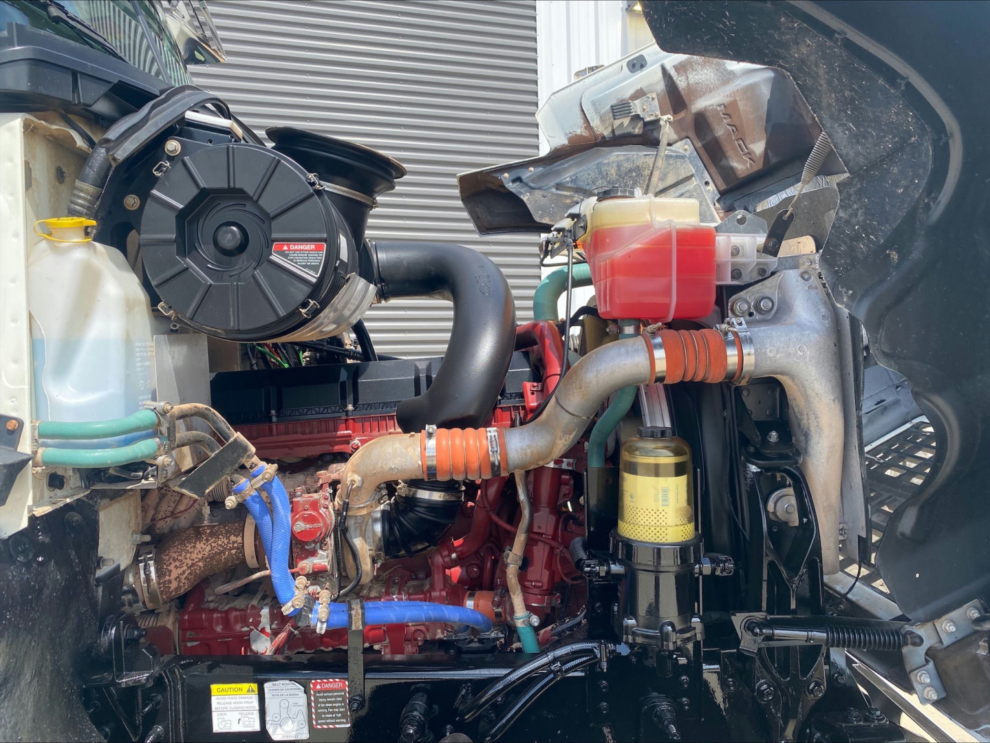 Mack PI64T engine bay showing coolant reservoir, air intake, hoses, and engine components.
