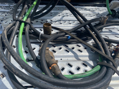 Truck component view showing tangled hoses and fittings on a perforated metal surface, with green and black hoses and a brass colored fitting.