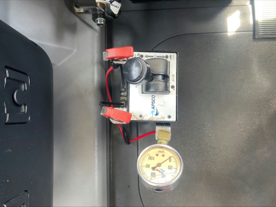 Mack PI64T cab interior showing air pressure gauge and battery disconnect switch with red clamps and wiring.